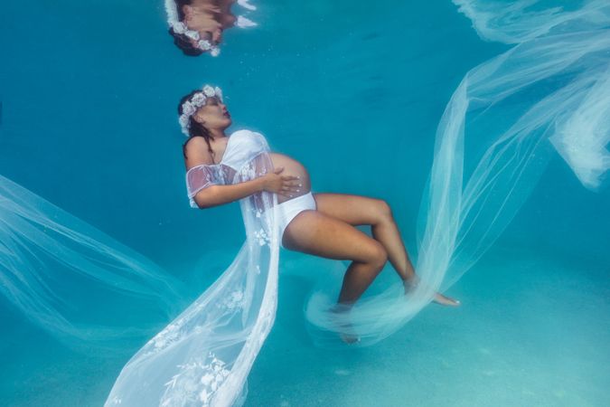 Pregnant woman in wreath and dress underwater