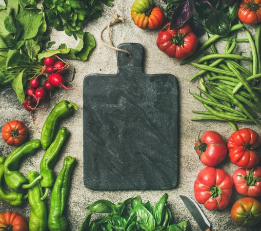 Fresh vegetables arranged with dark cutting board in center, square crop
