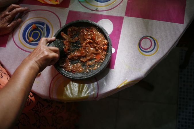 Person preparing red paste and spices to grind in mortar on table