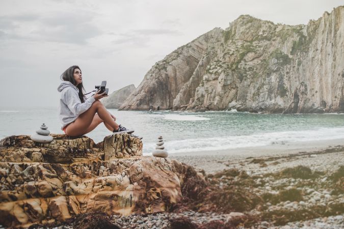 Woman with camera on shore near stones and water