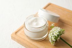 Jar with cream, allium flowers and board on plain background, closeup