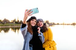 Casual women taking selfie on smartphone at sunny lake