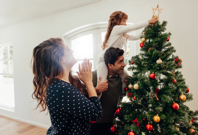 Young girl piggy-backing on father's shoulder to put star on top of tree