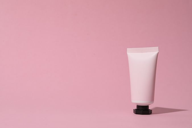 Pink tube with cream on pink background, space for text