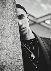 Monochrome shot of man in Africa necklace looking out behind wall