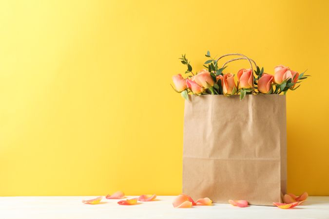 Paper bag with bouquet of orange roses on table against color background, space for text