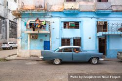 Side view of man riding a classic blue car beside blue building in Havana, Cuba 56Evd0