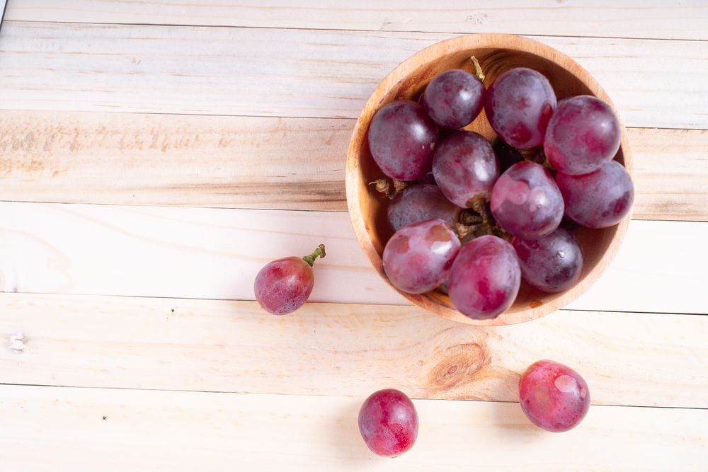 A bowl of red grapes sits on a wooden table