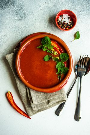 Top view of tomato soup in ceramic bowl on napkin with cutlery