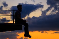 Out line of male sitting on ledge against a colorful dusk side