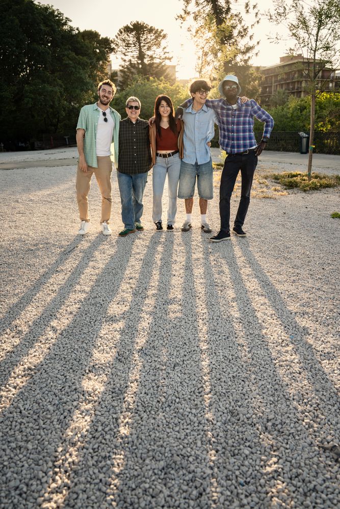 Full length portrait of a diverse group of friends standing together outdoors at sunset.