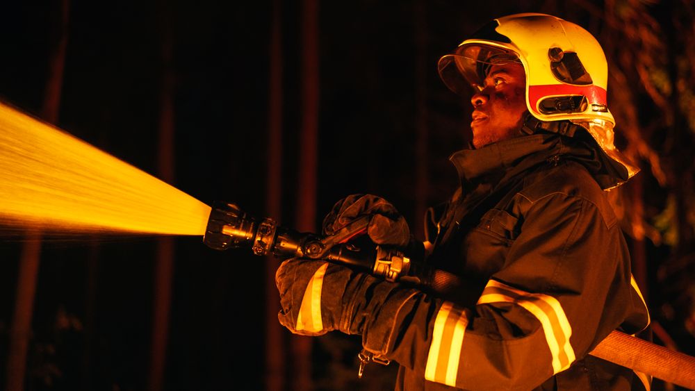 Calm and Focused Black Firefighter Extinguishing a Wildland Fire Deep in a Forest.
