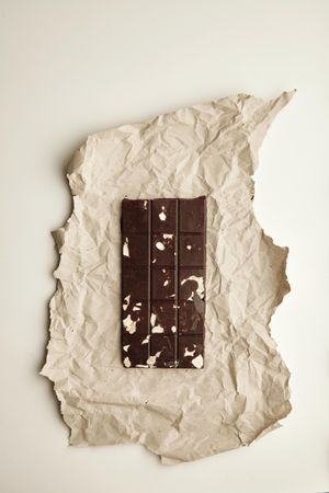 Chocolate bar with almonds on craft paper, top view
