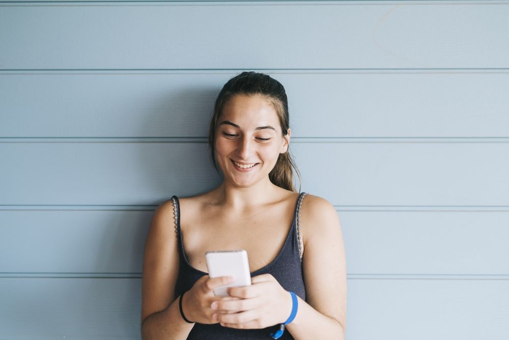 Teenage female texting on cell phone while leaning against wood paneled wall