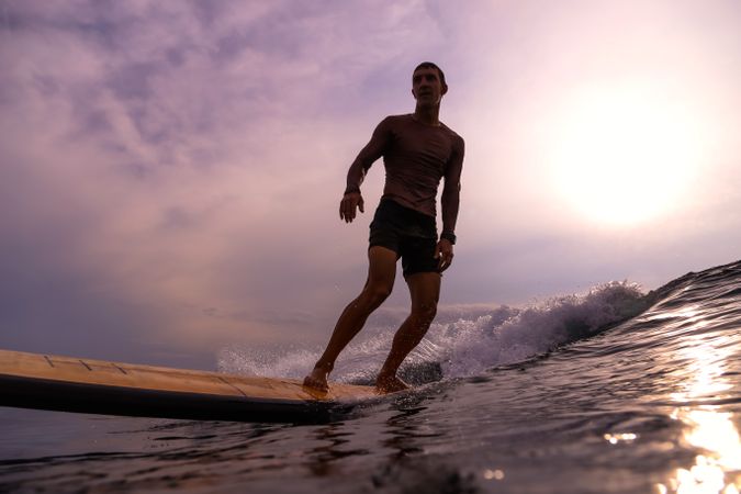 Man on surf board on waving water at sunset