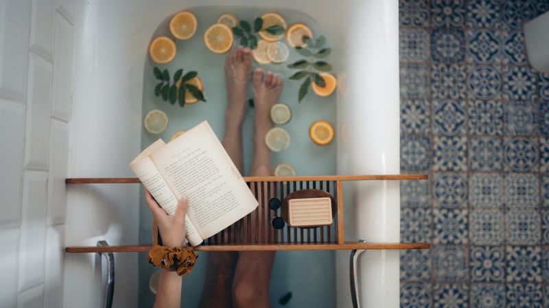 Top view of woman holding a book laying a bathtub