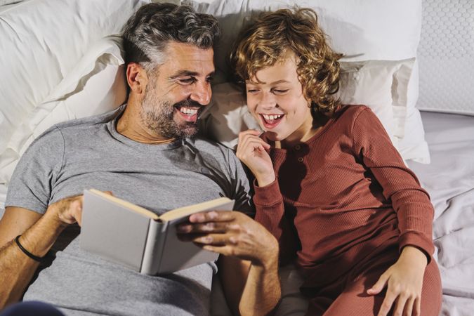 Laughing man and boy reading fairytale in bedroom