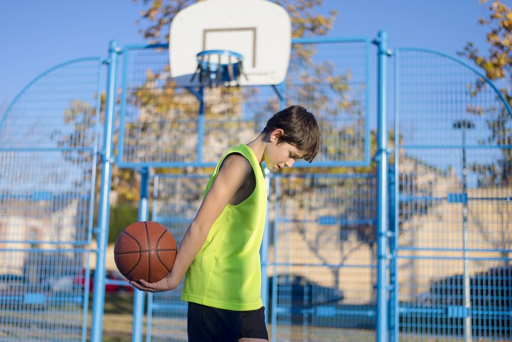Young basketball player standing on the court wearing a yellow sleeveless and holding a basketball
