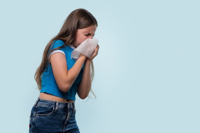 Girl sneezing into tissue, experiencing cold or allergy symptoms