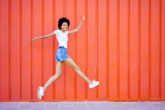 Side view of woman happily skipping in front of red wall