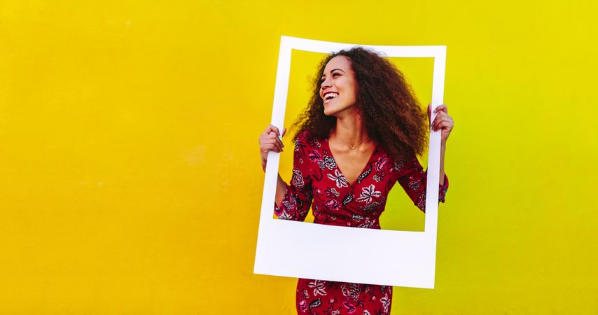 Happy young woman with curly hair looking away through a blank photo frame
