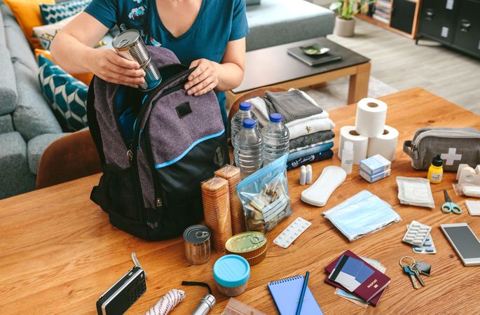 Woman putting cans of food to prepare emergency backpack