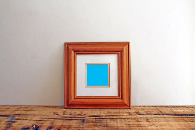 Square wooden picture frame on wooden desk mockup