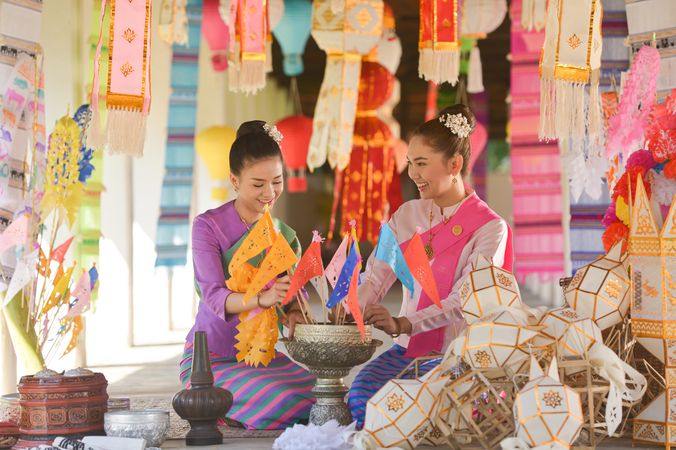 Two women in their traditional Thai outfit sitting on floor surrounded by decoration