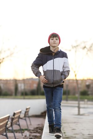 Unsmiling teenager wearing a red hat walking in city park