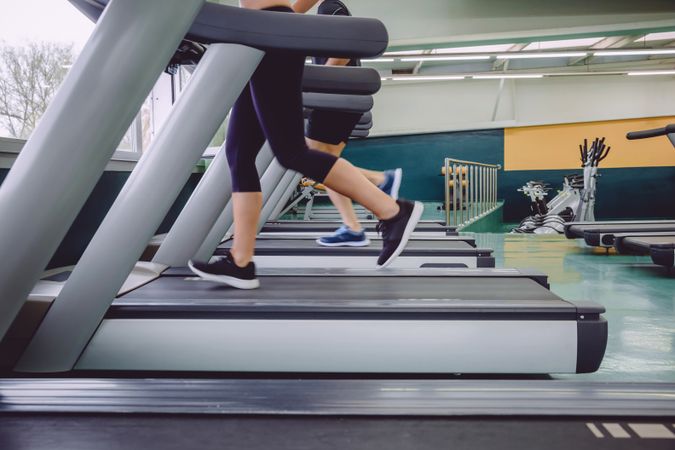 Feet of two people jogging on row on treadmills in gym