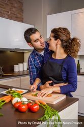 Loving couple in kitchen together as woman chops vegetables in kitchen 4AYyW4