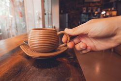 Crop person holding cup of coffee on table