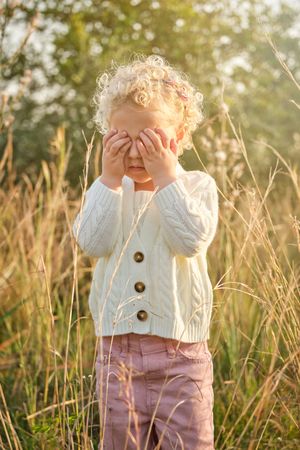 Adorable girl covering eyes with hands in sunny garden