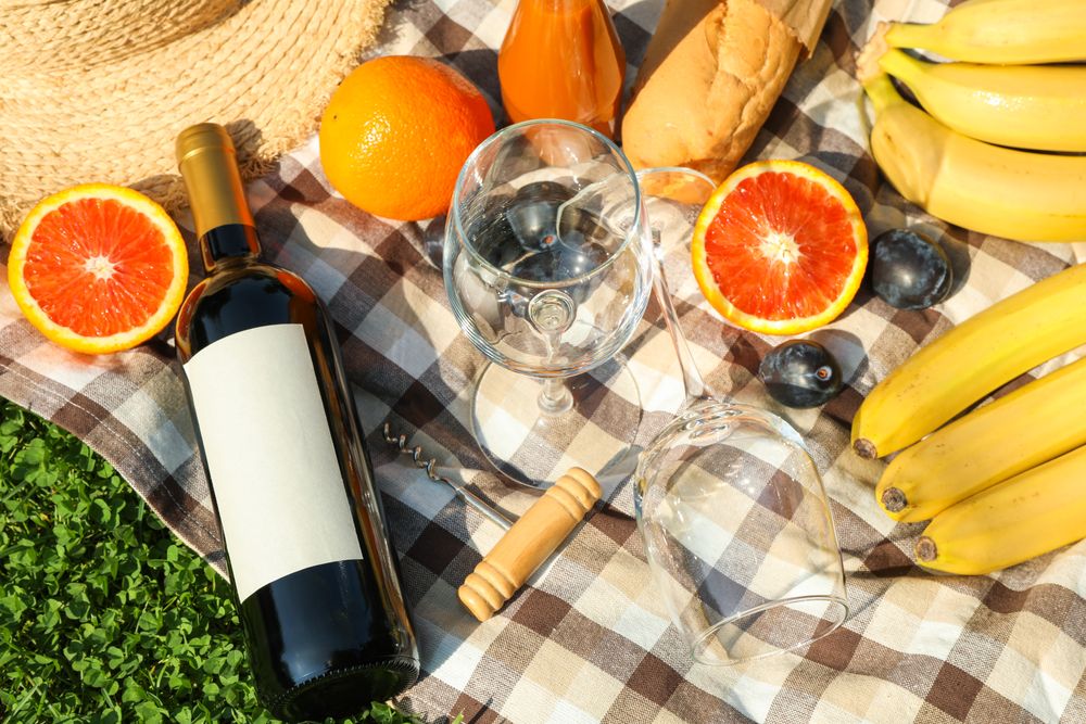 Bottle of wine, baguette, fruits, straw hat and towel on grass. Empty space