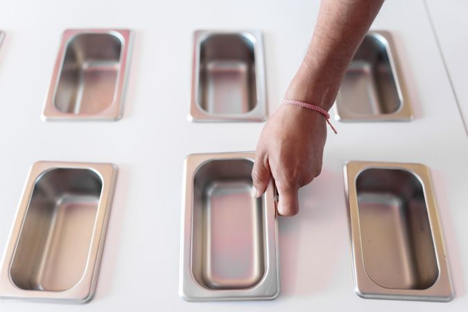 A hand of an ice-cream parlor worker is placing a clean metal tray