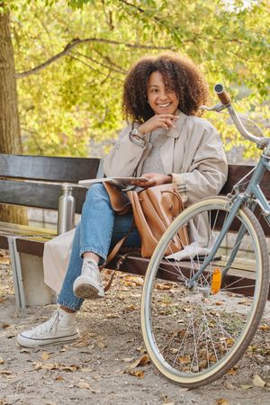 Smiling woman sitting on bench in park near bicycle