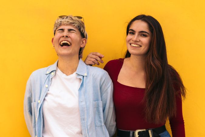 two women laughing on a yellow background