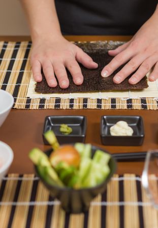 Hands of female chef ready to prepare sushi rolls, with fresh ingredients in the foreground, vertical