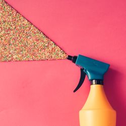 Spray bottle spraying sprinkles on pink background