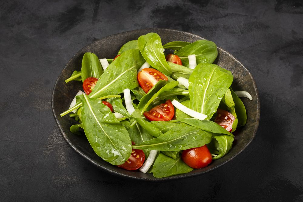 Arugula salad with tomatoes on dark background.