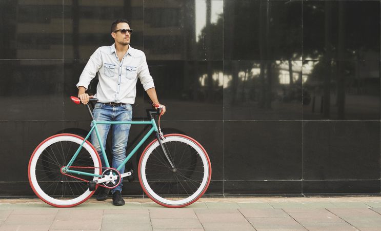 Male relaxing standing with his bike next to reflective wall outside