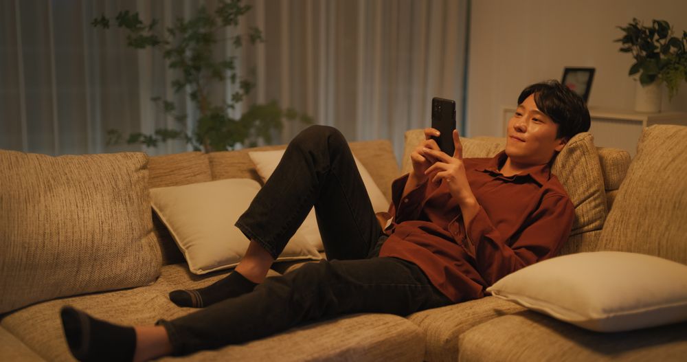 South Korean Young Man Enjoying His Leisure Time while Relaxing and Using a Smartphone.