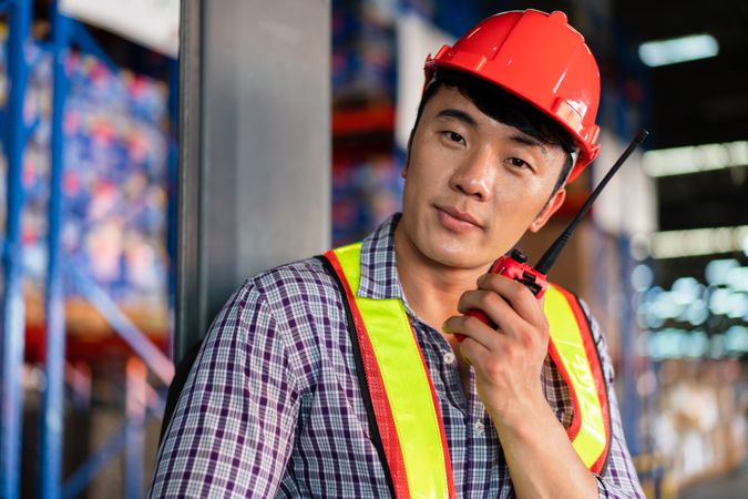 Smiling Asian warehouse worker with walkie-talkie.