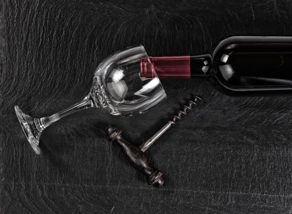 Overhead view of vintage corkscrew with red wine bottle and drinking glass on dark slate background