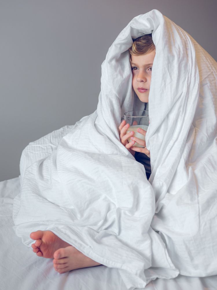 Little boy wrapped in blanket on bed