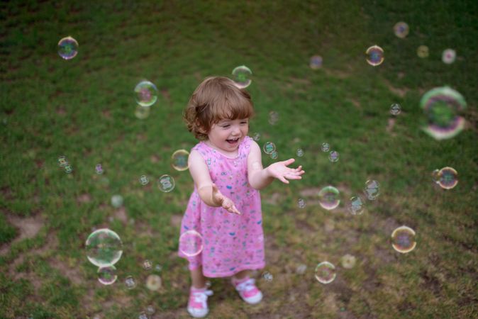 Joyful girl playing with colorful bubbles in grass