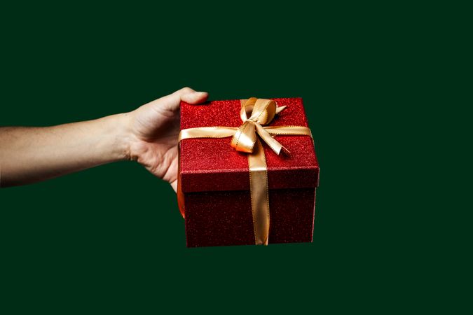 Hand holding a sparkling red Christmas gift box on a green background.