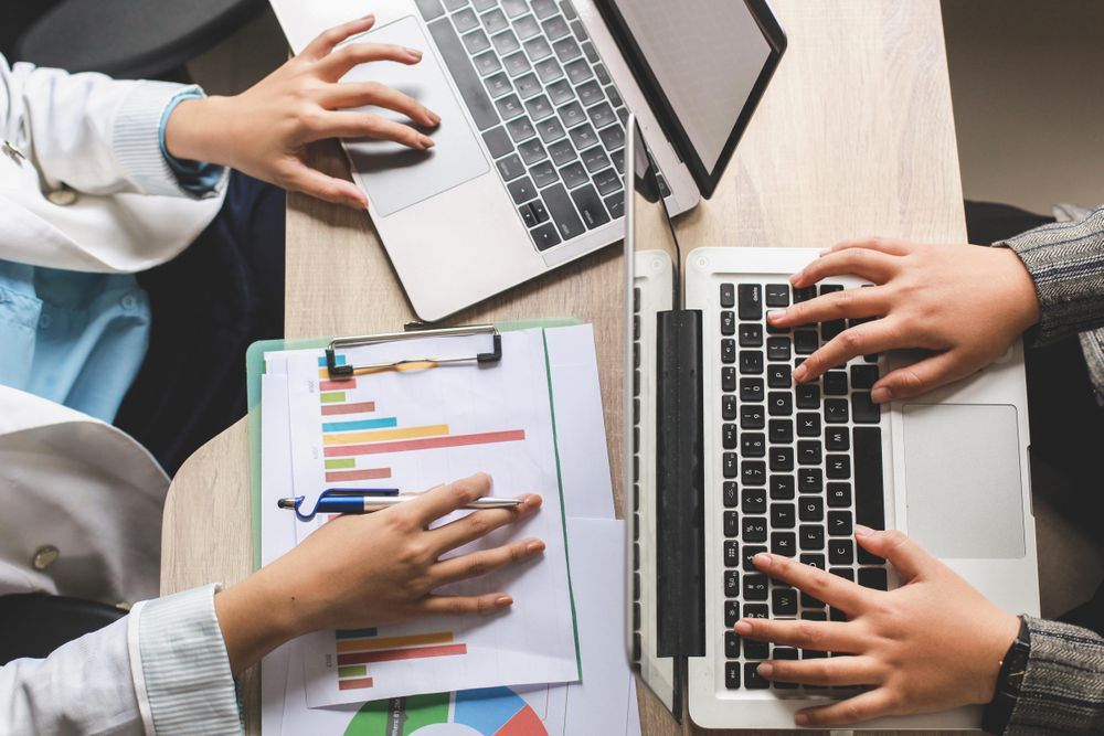 Two colleagues discussing pivot tables and using laptop in an office