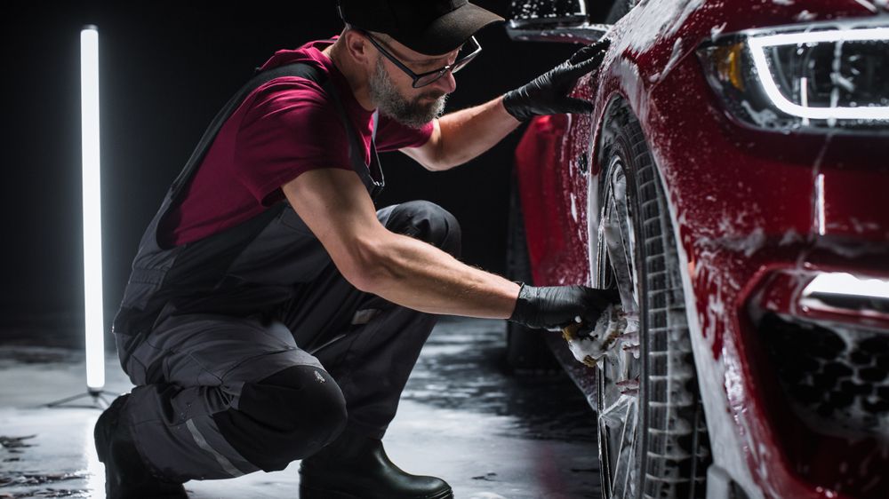 Portrait of an Adult Man Working in a Detailing Studio, Prepping a Factory Fresh American Sportscar for Maintenance Work and Car Care Treatment.