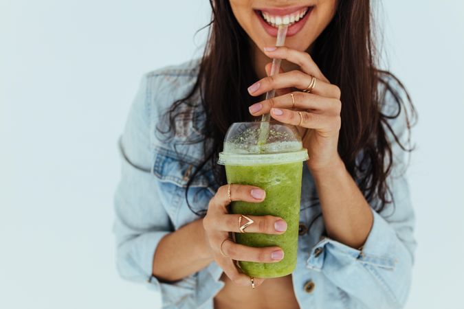 Close up of smiling woman drinking fresh juice with straw on light background